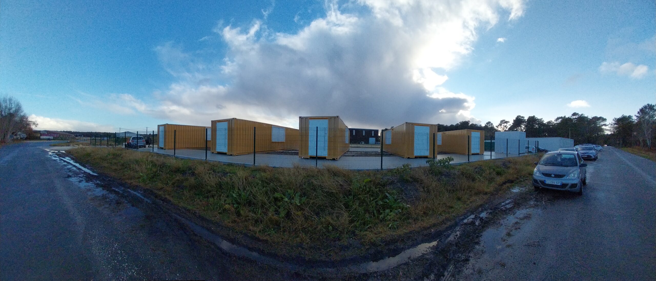 Photo où plusieurs containers transformés en local technique sont exposés derrière un grillage chez un client.